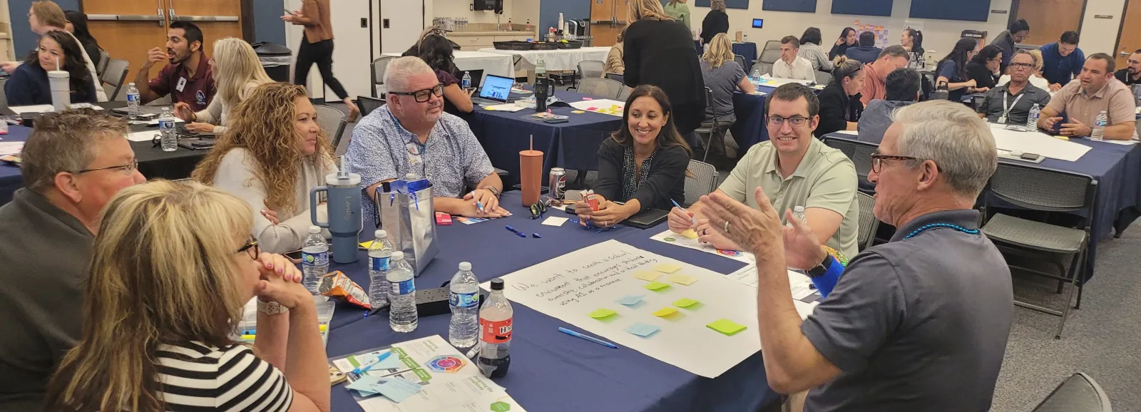 A team around a table covered in sticky notes listens as a colleague explains an idea